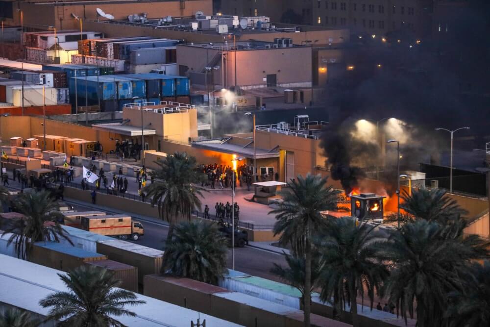 Nighttime urban scene with fires and smoke among buildings and palm trees.