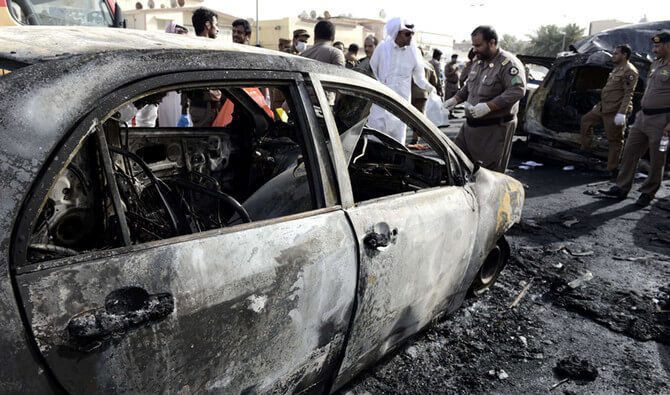 A burned-out car surrounded by people in traditional Middle Eastern clothing.