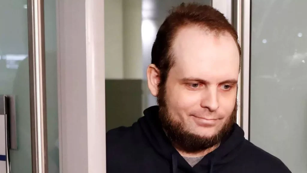 Man with a beard peeking from behind a door.