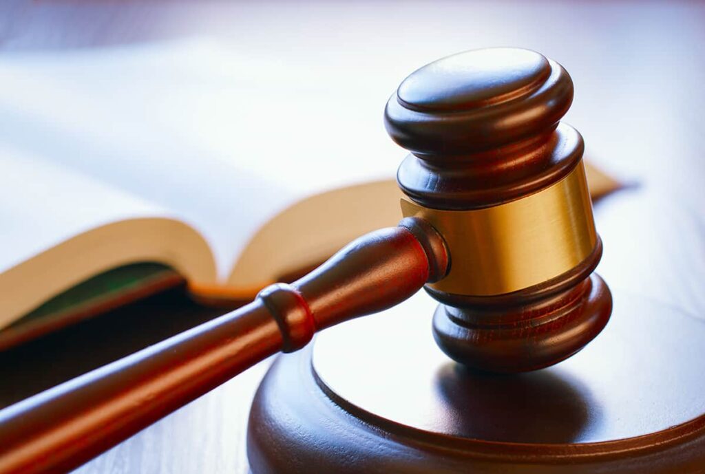 A wooden judge's gavel resting on its sound block with an open book in the background.