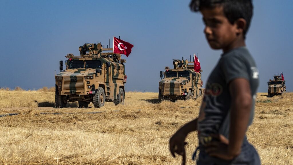 Turkish military vehicles with flag in a dry field under clear sky.