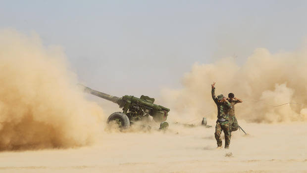 Soldier running near an artillery gun firing in a dusty desert.