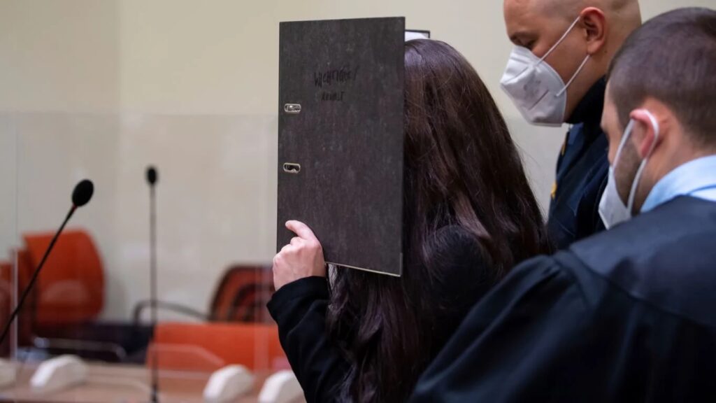 Person holding a black folder to cover their face in a courtroom.