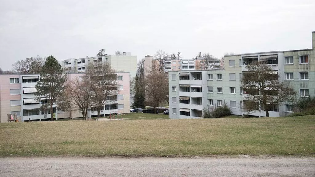 Two apartment buildings with grass and trees in front under a cloudy sky.