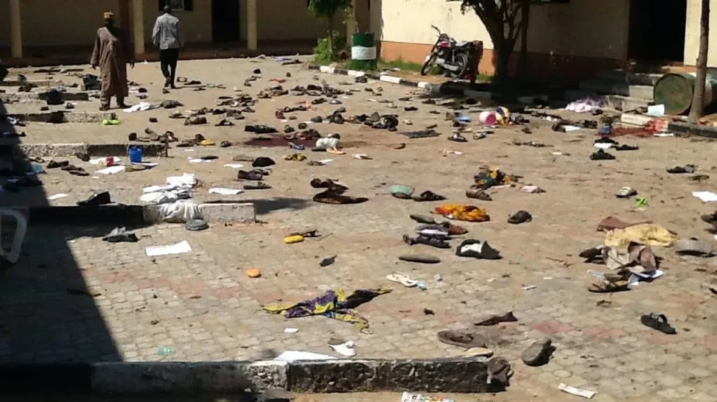 Scattered shoes and debris on a paved street with people in the background.