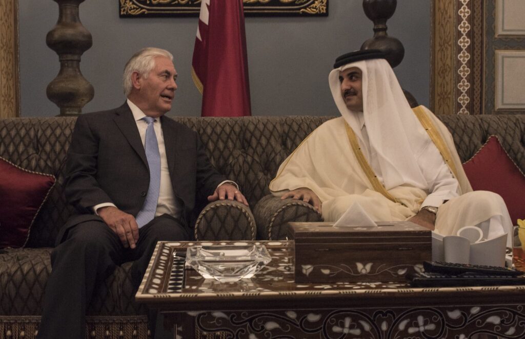 Two men in traditional attire sitting and conversing on a sofa.