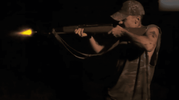 Man aiming a rifle in a dark setting.
