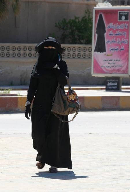 A woman in black attire carrying a basket walking outdoors.