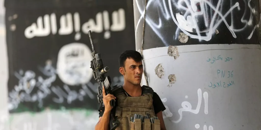 A soldier armed and standing in front of a wall with graffiti.