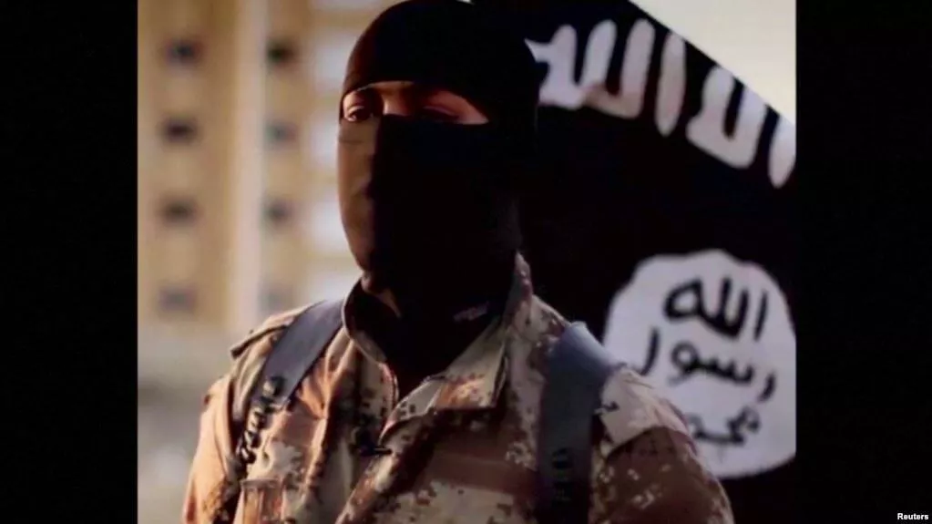 Masked militant in camouflage in front of a black flag.