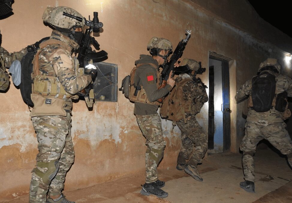 Military personnel in tactical gear entering a building during a night operation.