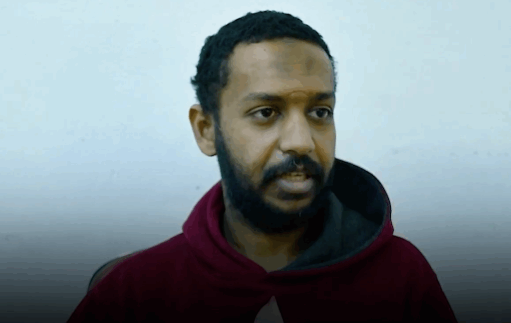 Man with beard and hoodie looking to the side indoors.