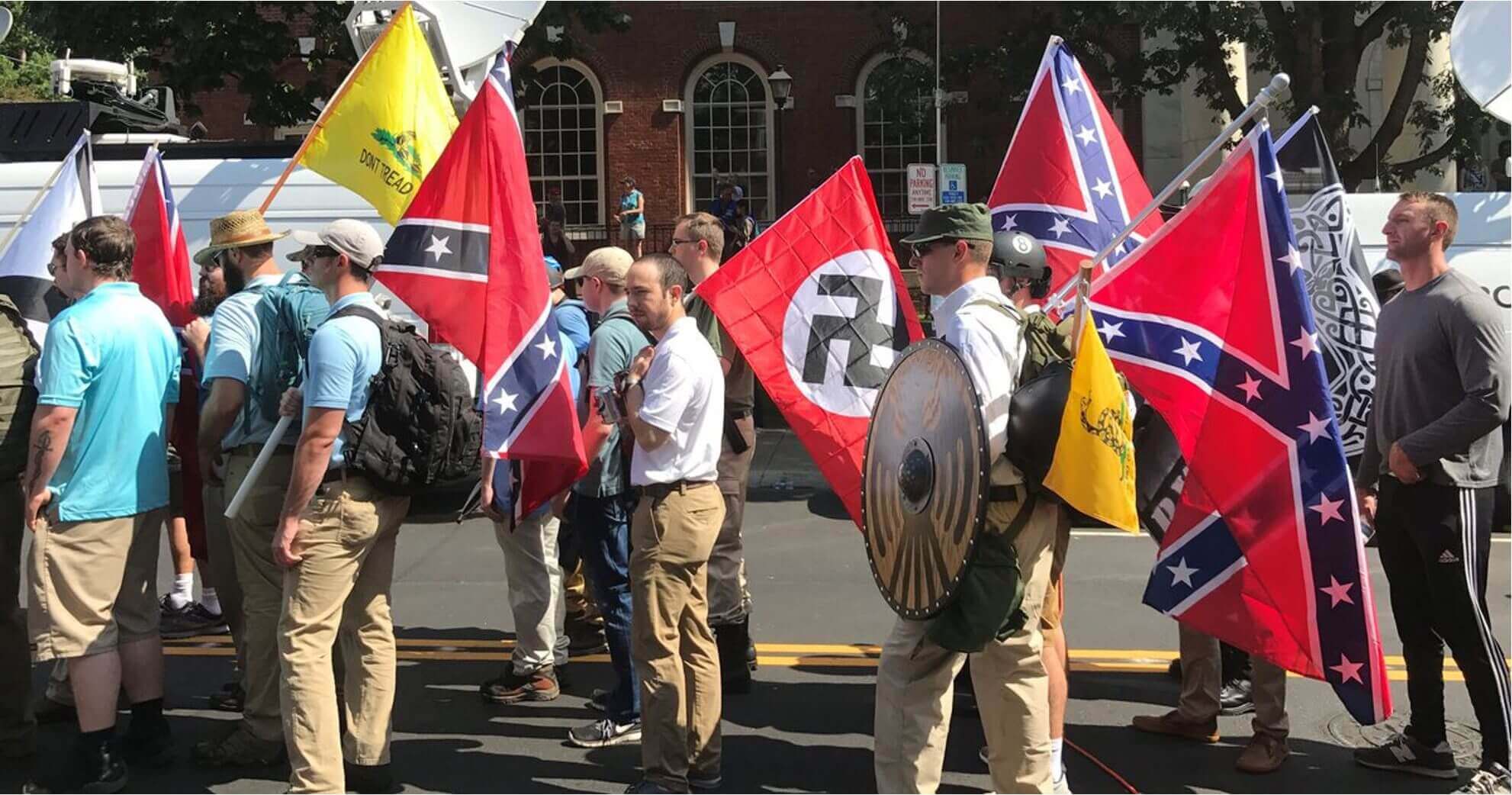 Group of men holding various controversial flags, including Nazi and Confederate flags.
