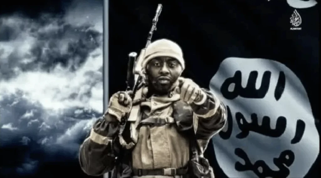 Soldier in tactical gear pointing forward, with a black flag in the background.