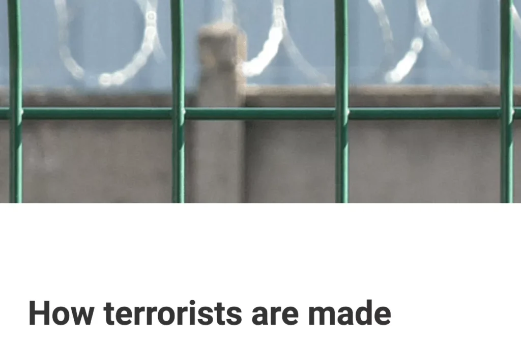 Barbed wire behind a green metal fence with a caption about terrorists.