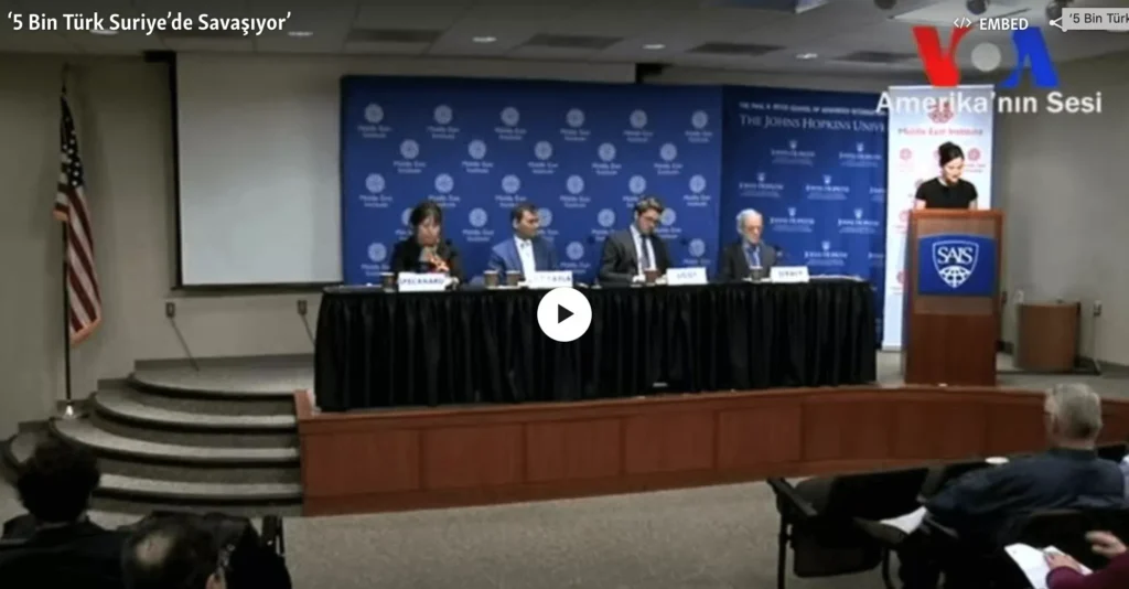 Panel discussion at a conference with four speakers seated behind a table.