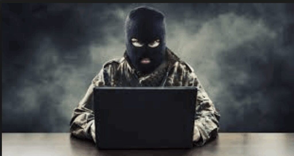 A masked individual using a laptop in a dark, foggy setting.