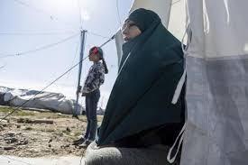 Two women outdoors, one wearing a black hijab, the other standing with a red headscarf.