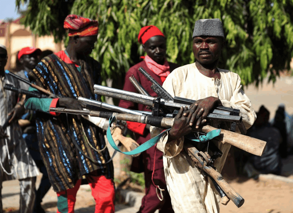 Armed men in traditional attire standing in a forested area.
