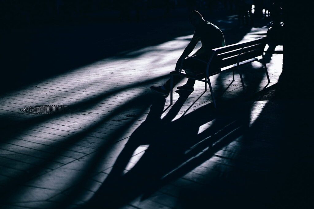 A person sitting on a bench with dramatic shadows and light patterns.