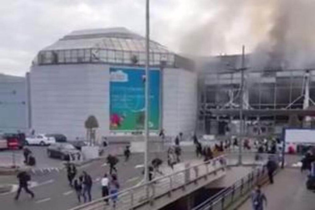 Smoke rises from a burning building as people evacuate the area.