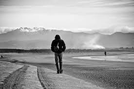 A person walks alone on a path with mountains in the background.