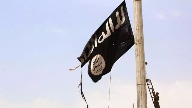 A black flag with white Arabic script flying against a clear sky.