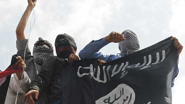 Masked individuals holding a black flag with white Arabic script.