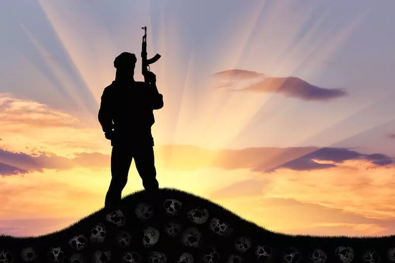 Silhouette of a soldier standing on a hill at sunset.