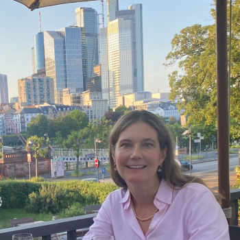 Molly_headshot-1 A woman smiling outdoors with city skyscrapers in the background.