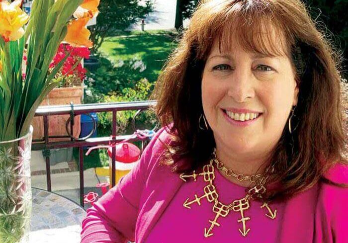 Smiling woman in a bright pink top sitting outdoors on a sunny day.