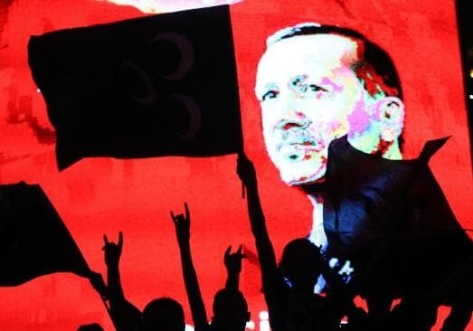 Silhouetted crowd with raised hands against a red background and a prominent male figure.