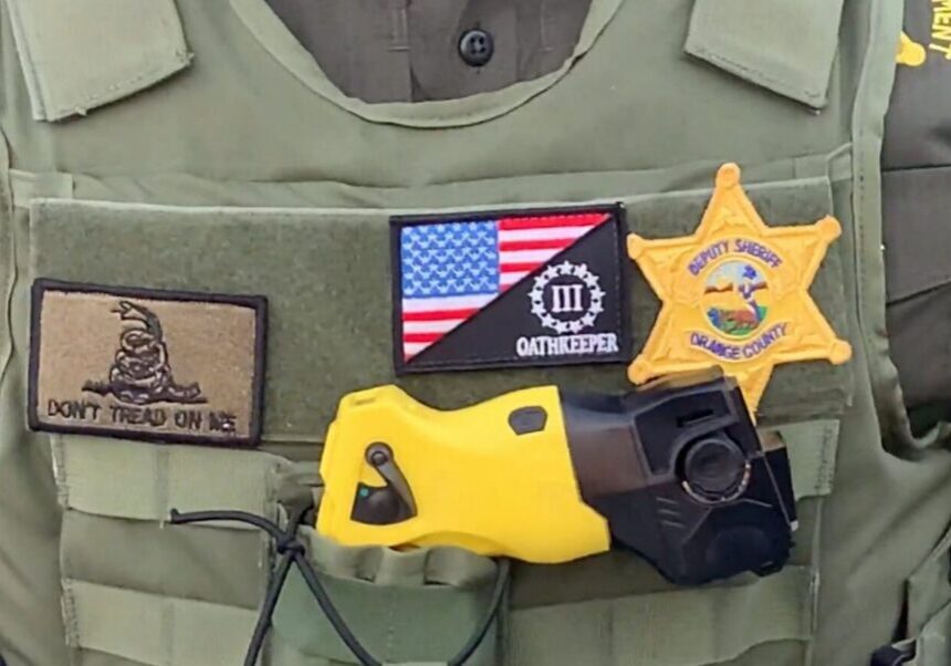 Tactical vest with patches, an American flag, and a yellow taser.