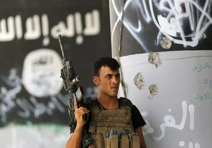 A soldier armed and standing in front of a wall with graffiti.