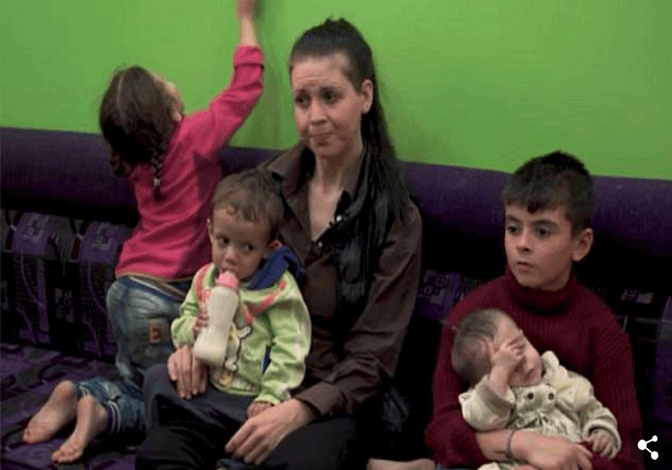 A woman sits on a couch with four children, two holding babies.