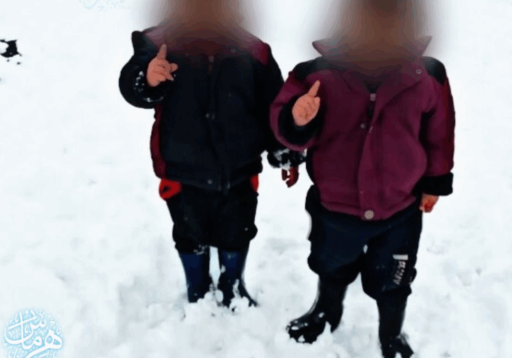 Two children playing in the snow wearing winter jackets and boots.