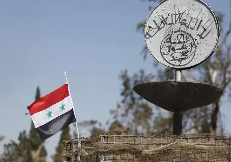 Syrian flag waving near a memorial with Arabic inscription.