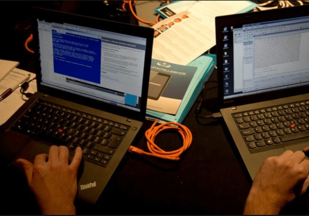 Two laptops connected with an orange Ethernet cable showing a Windows error screen.