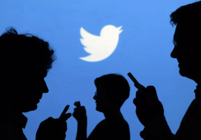 Silhouettes of people using phones with a large Twitter logo in the background.