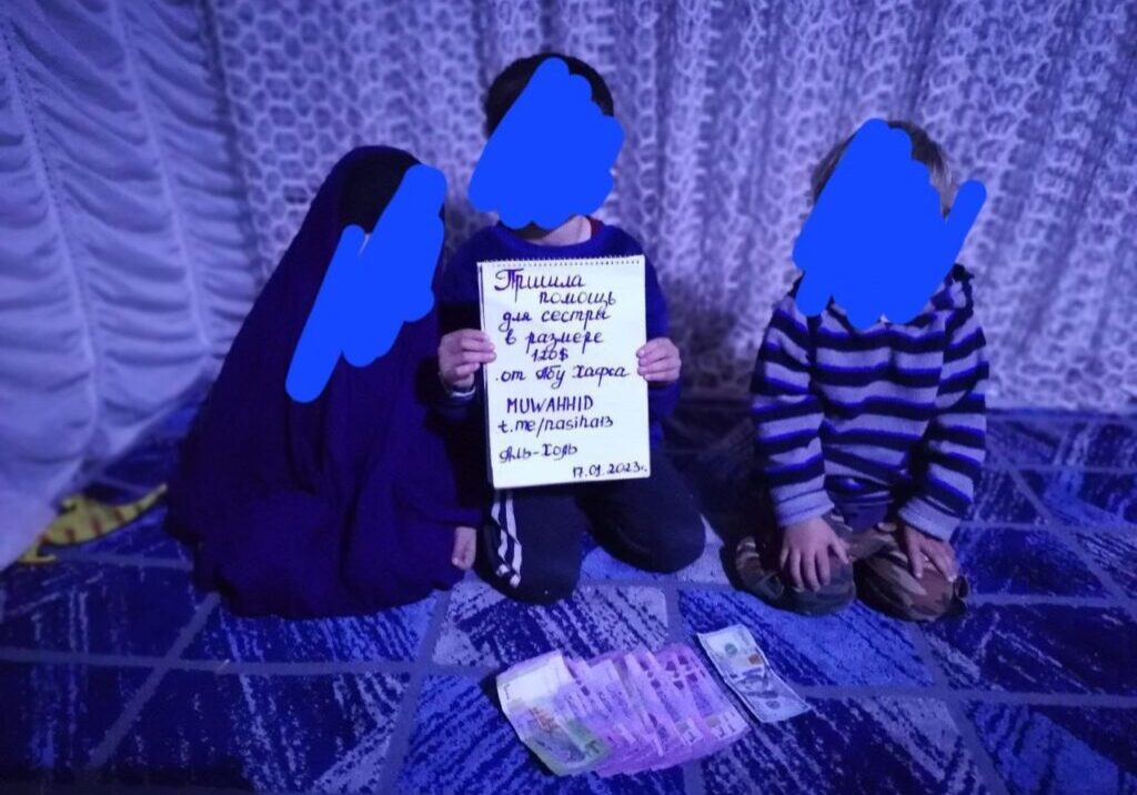 Three people sitting on the floor holding a sign with handwritten text in dim purple lighting.