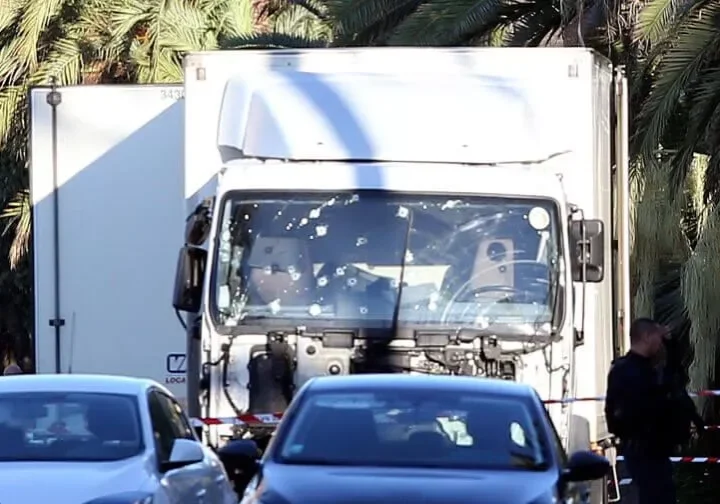 Truck windshield riddled with bullet holes on a busy road.