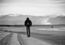A person walks alone on a path with mountains in the background.