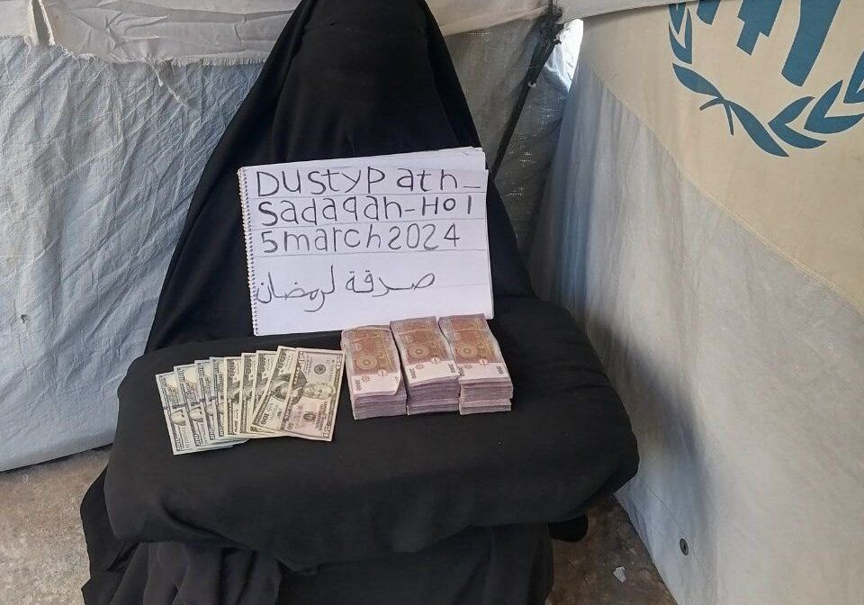 Person covered in black with handwritten sign and money displayed.