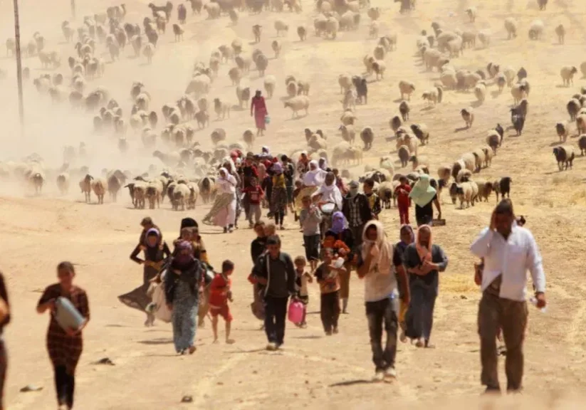 A large group of people walking through a dusty, arid landscape.