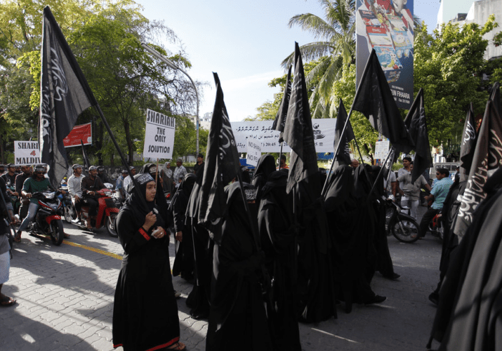 Women dressed in black robes holding black flags during a public gathering.